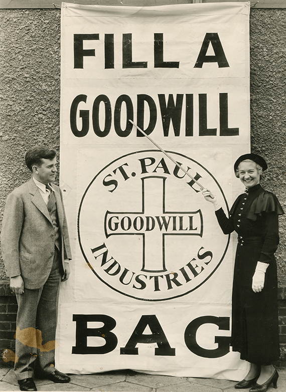Photo of a man and woman in front of a large banner that states "Fill a Goodwill Bag" 