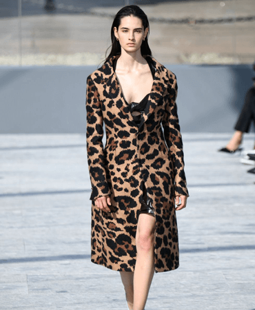Photo of model walking down a runway in a leopard print long coat.