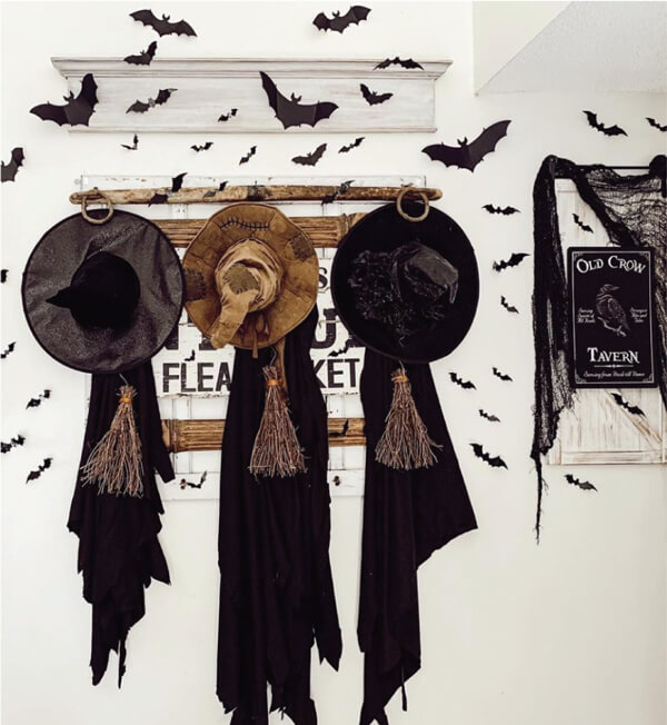 Photo of witches' hats on a hanging coat rack with black bat cutout sillouttes on a white wall. 