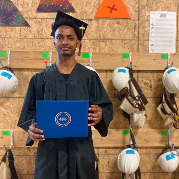 Dagme in his cap and gown holding his diploma.