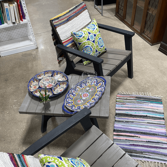 A lawn chair with pillows on it and a side table next to it with serving dishes.