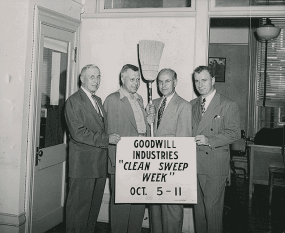Photo of four men holding a sign and a broom that states "Clean Sweep Week"