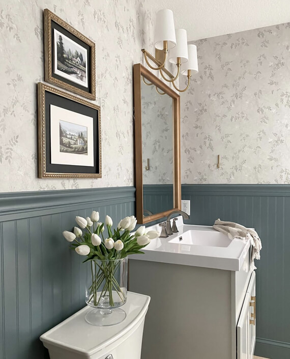 Photo of a bathroom sink, mirror, flower and framed pictures.