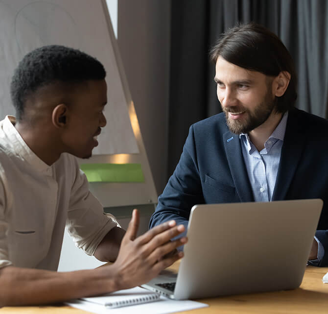 Photo of youth speaking with an adult at a table with a laptop open