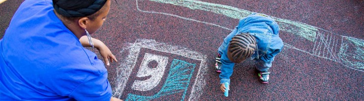 Photo of an adult and a child drawing the Goodwill logo in chalk on asphalt