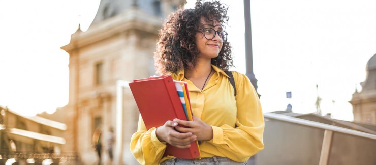 Woman with glasses standing outside holding a binder and some notebooks.