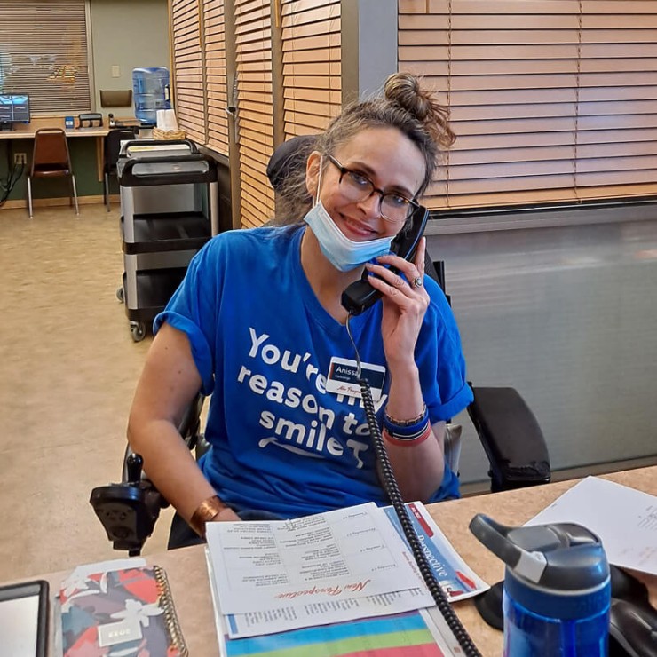 A female wearing glasses, a blue shirt and holding a phone to her ear.